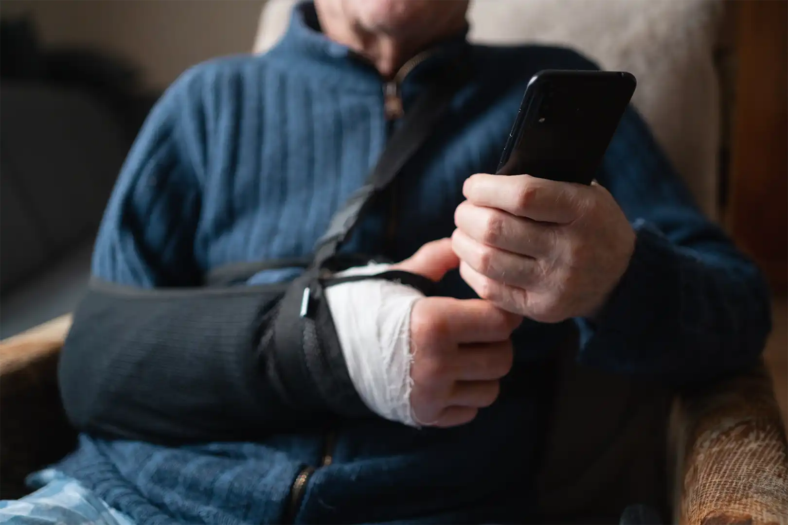 A man is sat on his sofa with a broken arm whilst using his phone.